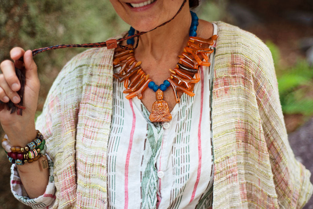 Model wearing orange shapes of resin coral necklace with blue recycled glass African beads and a Buddha as the center piece. Cristina Tamames Jewelry Designer