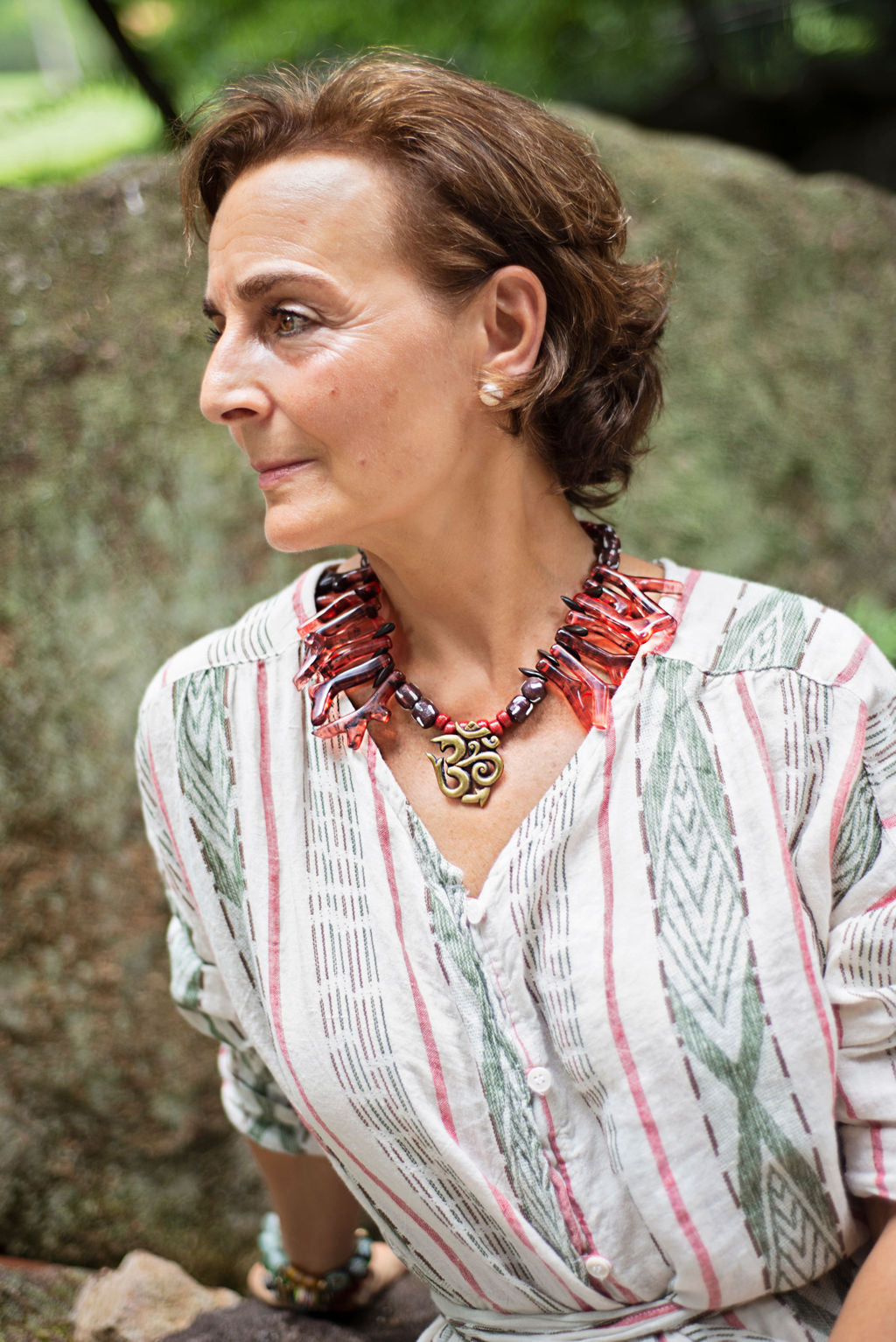 Model wearing red shapes of resin coral necklace with Nepalese Om center piece. Cristina Tamames Jewelry Designer