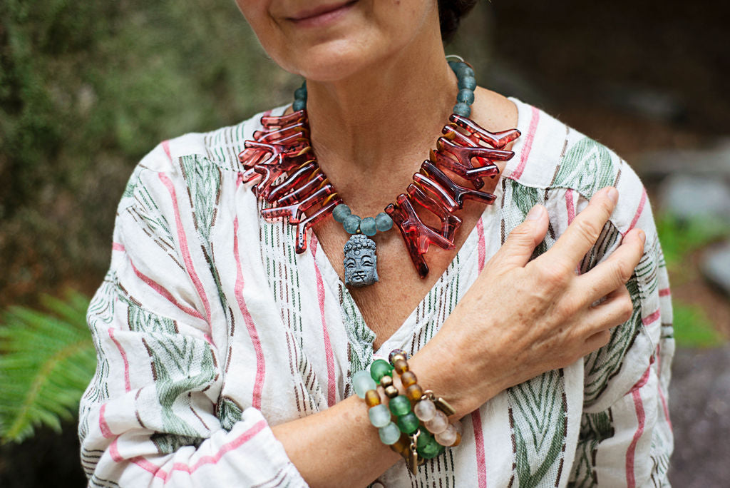 Model wearing red shapes of resin coral necklace with blue recycled glass African beads and a Buddha as the center piece. Cristina Tamames Jewelry Designer