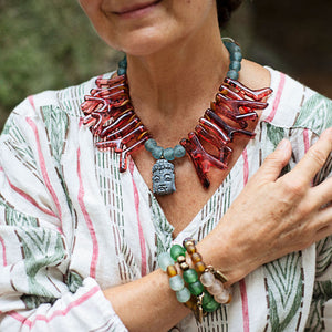 Model wearing red shapes of resin coral necklace with blue recycled glass African beads and a Buddha as the center piece. Cristina Tamames Jewelry Designer