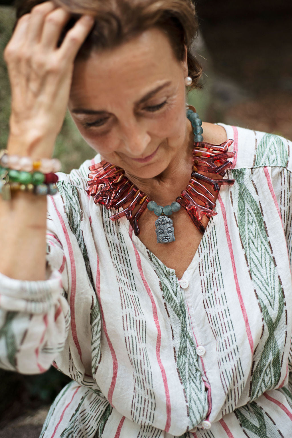 Model wearing red shapes of resin coral necklace with blue recycled glass African beads and a Buddha as the center piece. Cristina Tamames Jewelry Designer