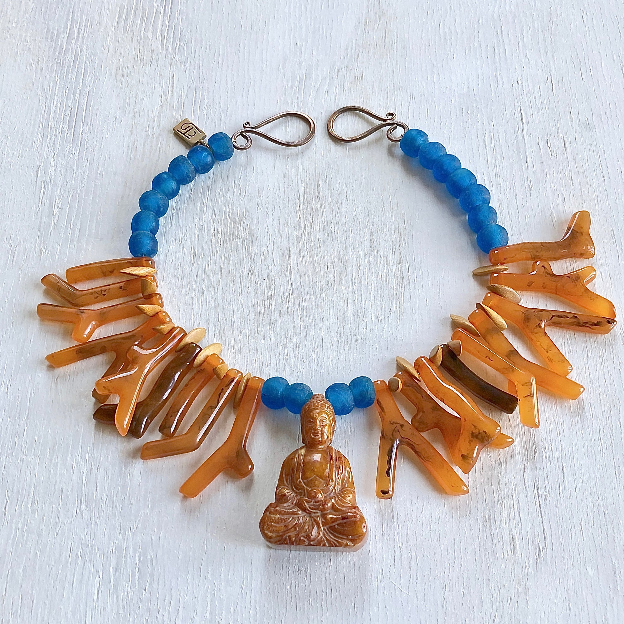 Orange shapes of resin coral necklace with blue recycled glass African beads and a Buddha as the center piece. Cristina Tamames Jewelry Designer